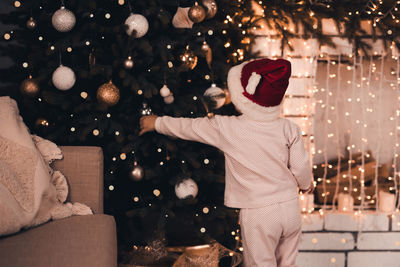 Rear view of girl touching christmas tree at home