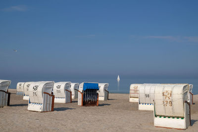 Hooded chairs on beach and sailboat against blue sky