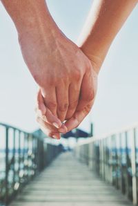 Cropped hand of couple holding hands on pier