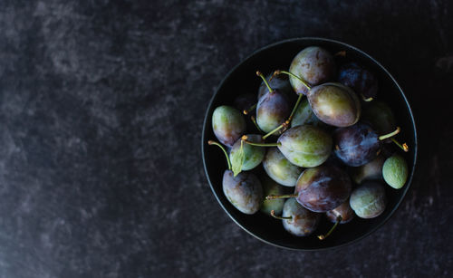 Overhead shot of a bowl of fresh plums against a black background.