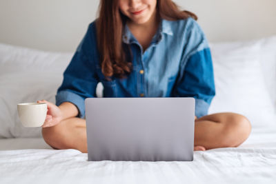 Midsection of woman using laptop while lying on bed at home