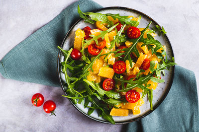 Close up of salad of orange, cherry tomatoes and arugula on a plate on the table top view