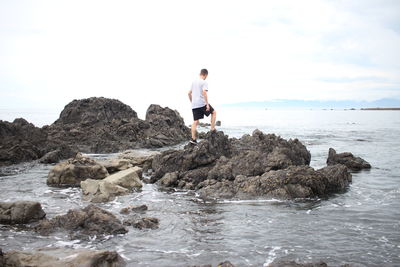 Man standing on rock at beach against sky