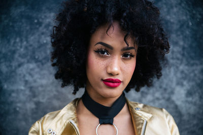 Fashionable young woman with curly hair against wall