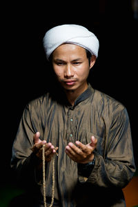 Portrait of young man standing against black background