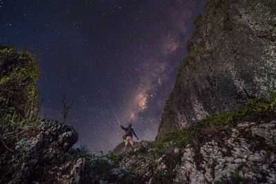 Low angle view of man standing on mountain against star field at night