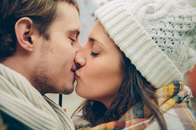 Side view of couple wearing warm clothing while kissing under umbrella in city