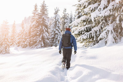 Rear view of man walking on snow covered field