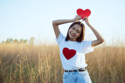 Woman holding heart shape while standing on field
