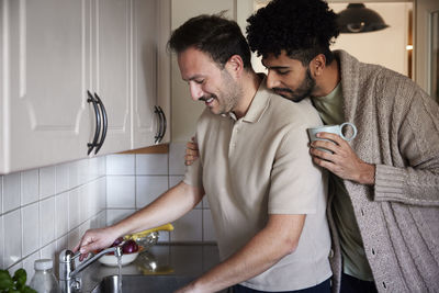Gay couple washing dishes and drinking coffee at home
