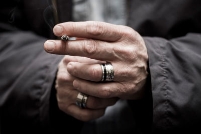 Midsection of man holding cigarette while sitting outdoors