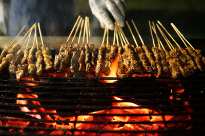 Cropped hand of vendor cooking meat on barbecue at market