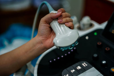 Close-up of hand holding ultrasound machine button with gel on it