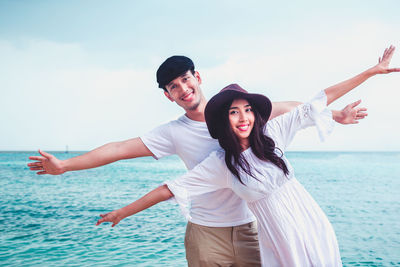 Full length of smiling young couple in sea against sky
