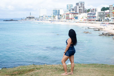 Beautiful woman with curly hair standing on a hill looking at the immense sea and the city. 