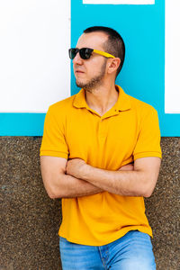 Young man wearing sunglasses standing against wall