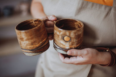 Woman potter holding mugs made by hand from clay