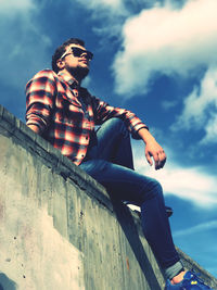 Low angle view of young man sitting against sky