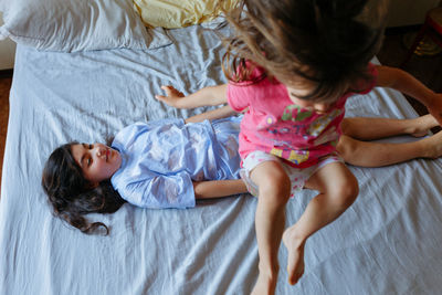 Hugh angle view of girl lying on the bed and other child jumping over