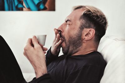 Mature man yawning while sitting on bed at home