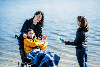 Happy family, mother, daughter and son with cerebral palsy spending time together on the river bank