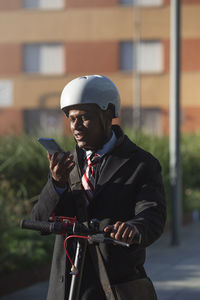 Young latin businessman driving electric motorcycle in the city street and talking on the phone.