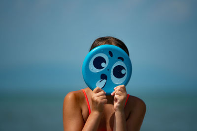 Cute girl holding smiley face against sky