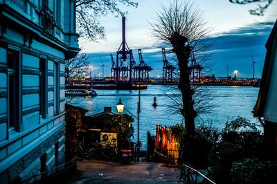 Illuminated buildings by river against sky at dusk