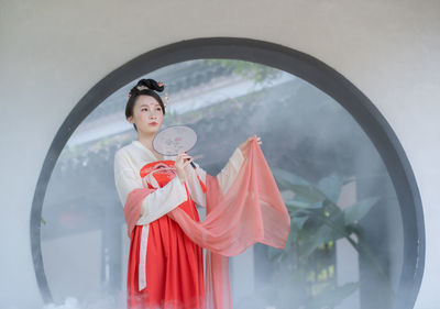 Portrait of young woman with red umbrella standing against white background