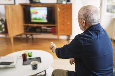 Rear view of senior man changing channels at home