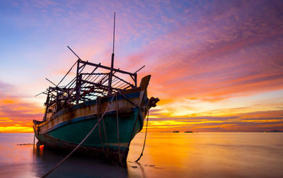 Boat moored in sea against sky during sunset