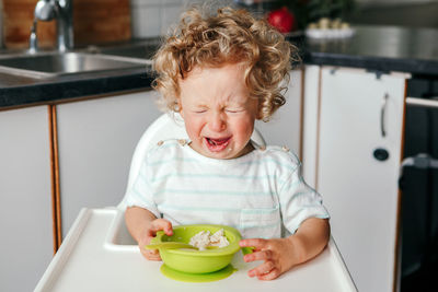 Crying caucasian kid boy with cereal puree. toddler screaming in tantrum. terrible two. 