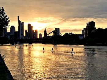 Silhouette city by river against sky during sunset