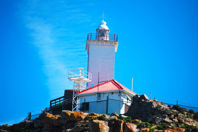 Low angle view of lighthouse by building against clear blue sky