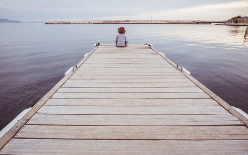 Rear view of woman on pier at sea against sky