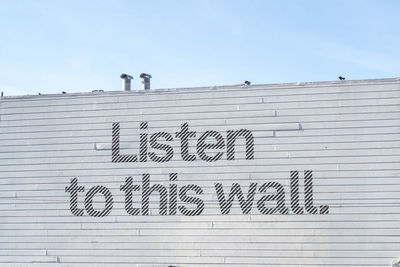 Low angle view of text on wall against clear sky