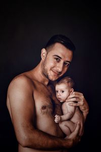 Portrait of shirtless father with baby against black background