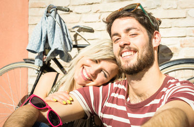 Portrait of young couple smiling while sitting against bicycle