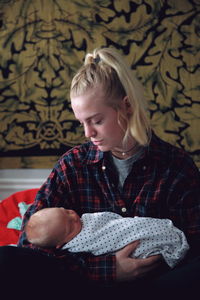 Woman holding baby while sitting on bed