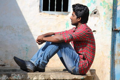 Side view of a man sitting against wall