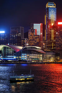 Illuminated bridge over river by buildings against sky at night