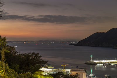 High angle view of illuminated city by sea at sunset