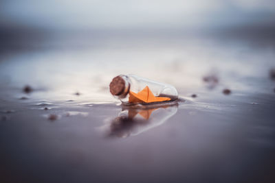 Miniature origami ship in bottle standing on sand at sunrise