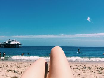 Low section of woman on beach against blue sky