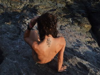 High angle view of shirtless young woman sitting on rock