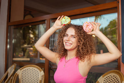 Portrait of beautiful curly young woman in cafe on summer terrace, delicious colorful donuts, 