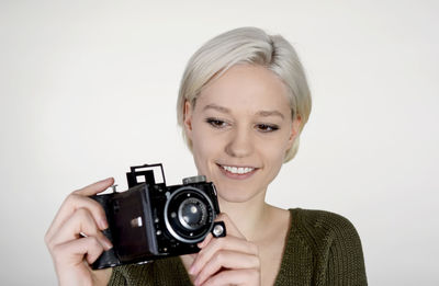 Portrait of smiling woman holding camera against white background