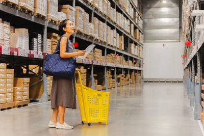 Woman with cart looking for houshold goods on a warehouse.