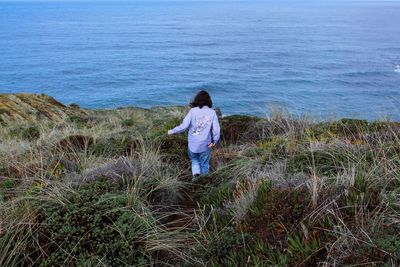 Rear view of woman amidst grass against sea