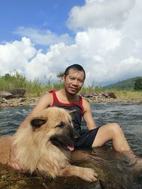 Portrait of young man with dog on field against sky